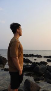 Man standing on rocky shore looking out at the ocean.